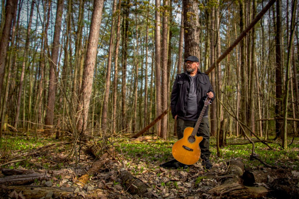 Jamie Haight in the woods with a guitar