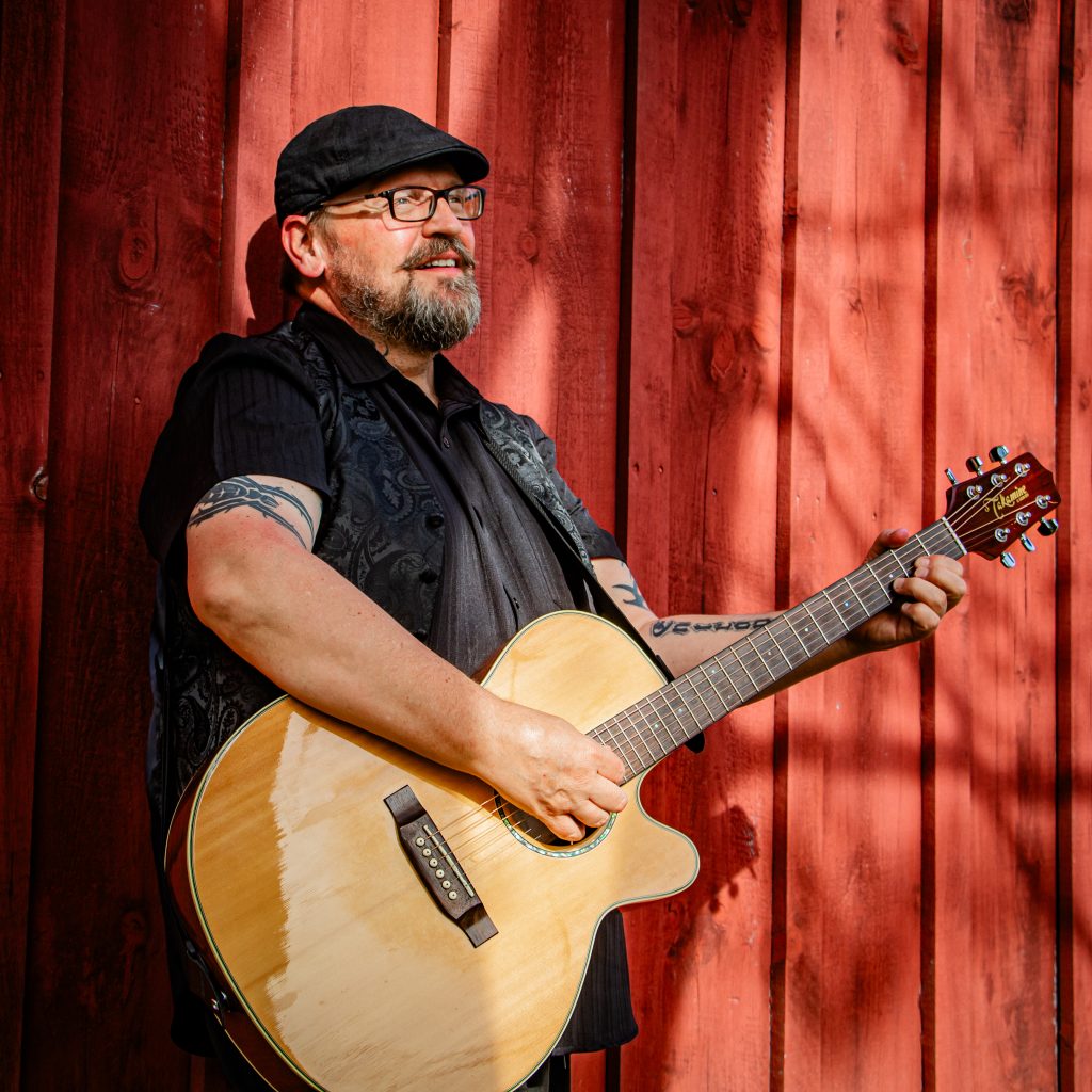 Jamie Haight with guitar standing against red wall